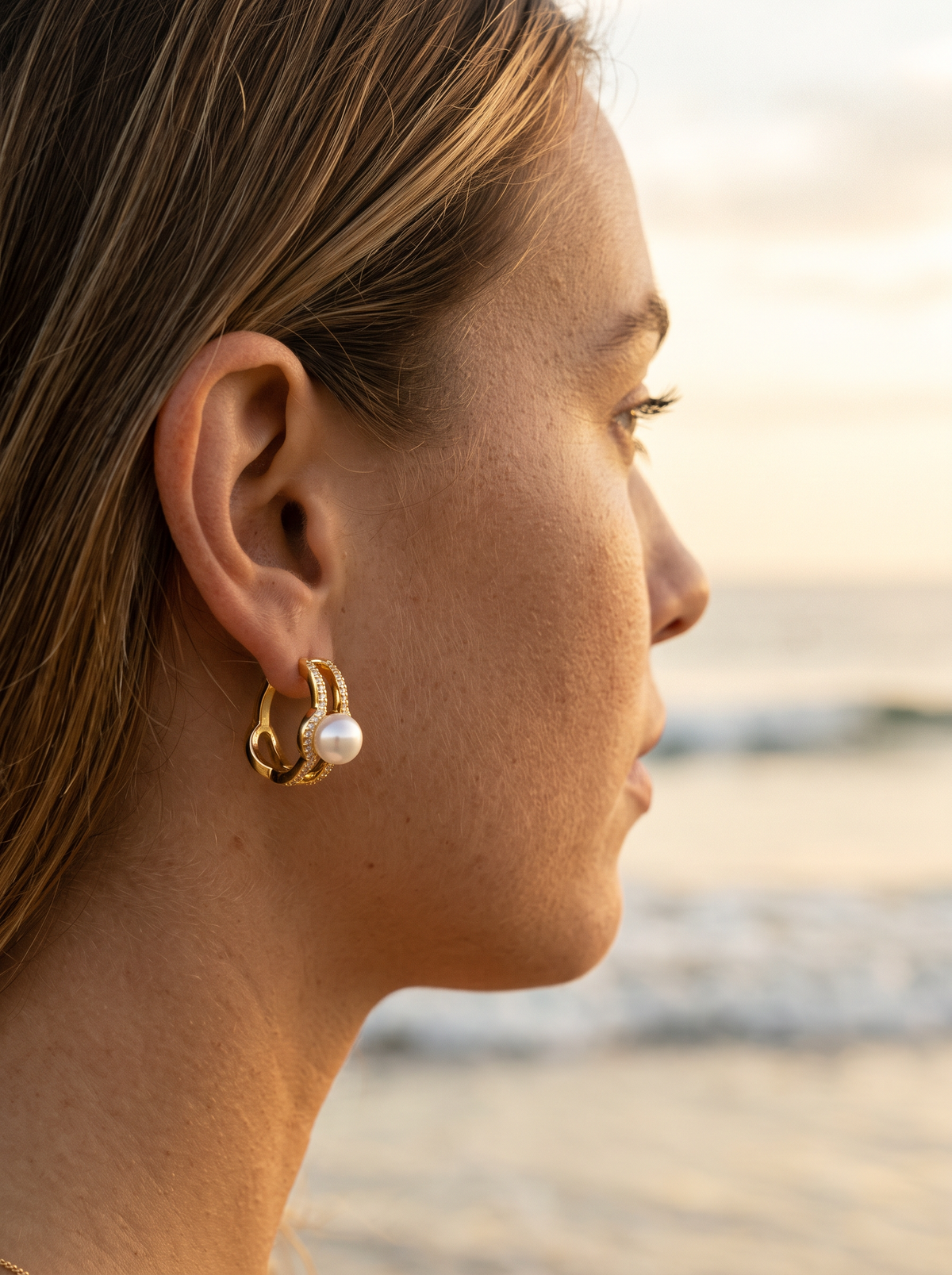 Argollas Elegance con perla puestas en la oreja, playa al atardecer | Buono Joyas