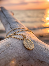 Cadena con San Benito sobre madera frente al mar al atardecer | Buono Joyas
